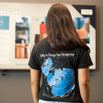 A woman viewed from behind wearing a black t-shirt with a large blue and white map graphic on the back, featuring the text 'A Map to Change Your Perspective' and 'WOODS HOLE OCEANOGRAPHIC INSTITUTION'.