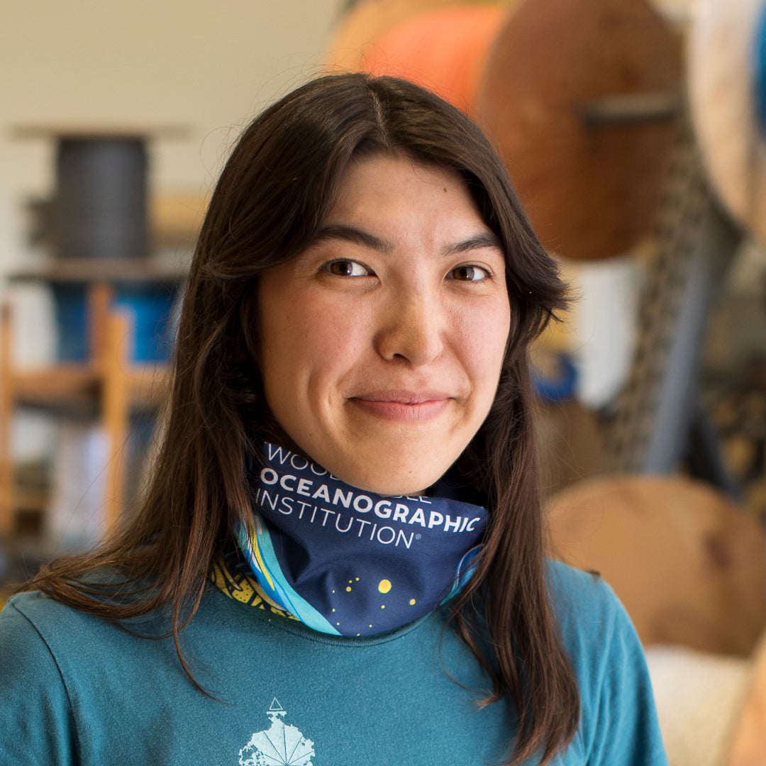 A woman with long dark hair wearing a blue bandana around her neck and a blue t-shirt, with the words 'WORLD OCEANOGRAPHIC INSTITUTION' visible on the bandana.
