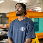 Man wearing a navy blue t-shirt with a white WHOI Classic Seal Logo on the front left chest in a lab.